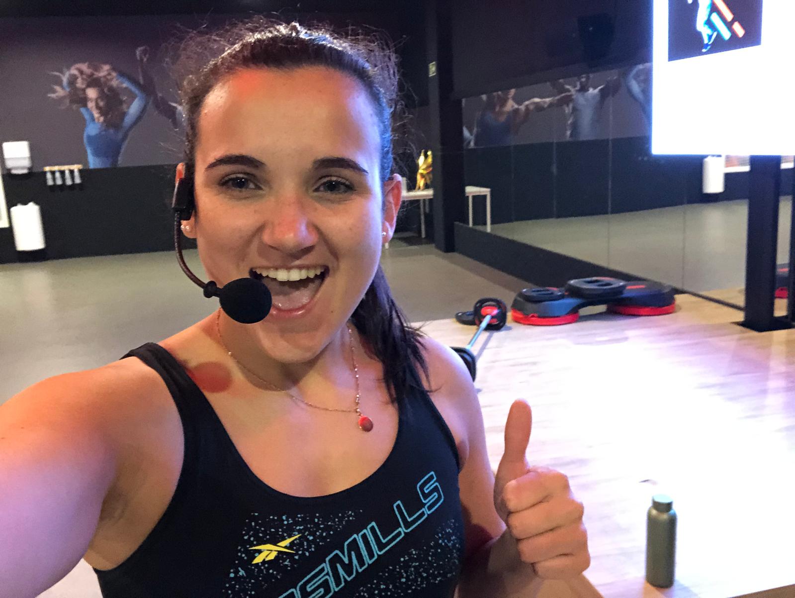 Miriam smiling in a fitness studio while wearing her instructor headset